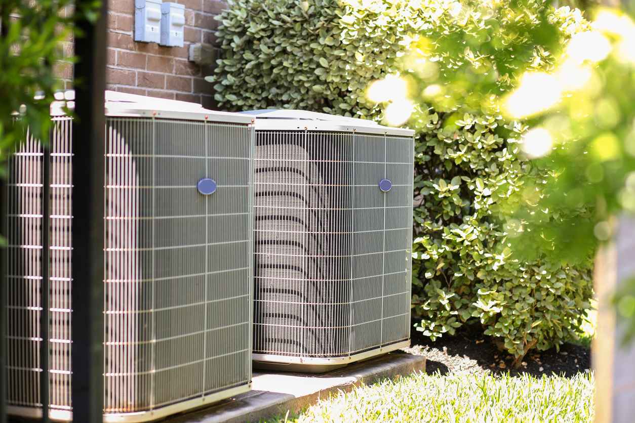 Air conditioner unit outdoors in side yard of a brick home in hot summer season.