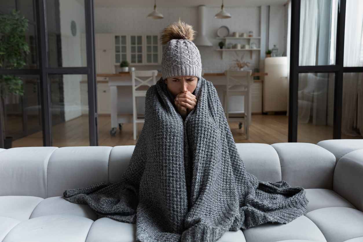 Female sitting on the couch feeling cold due to cold air blowing from the furnace