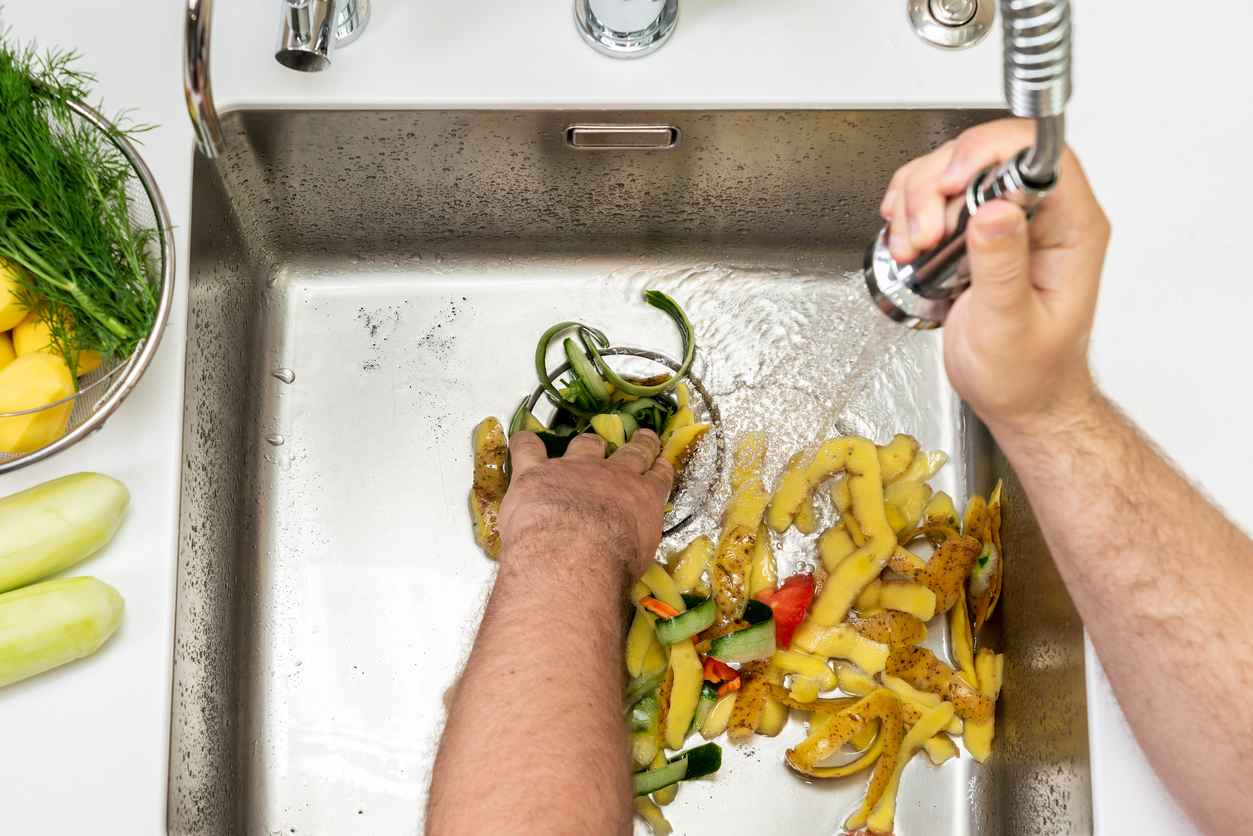 Food waste in the dispenser hole in the kitchen sink and a jet of water.