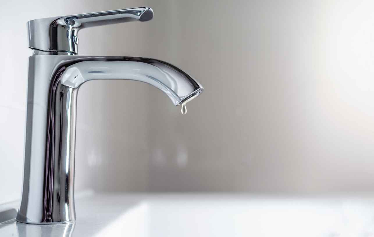 Faucet with a drop of water against a white sink.