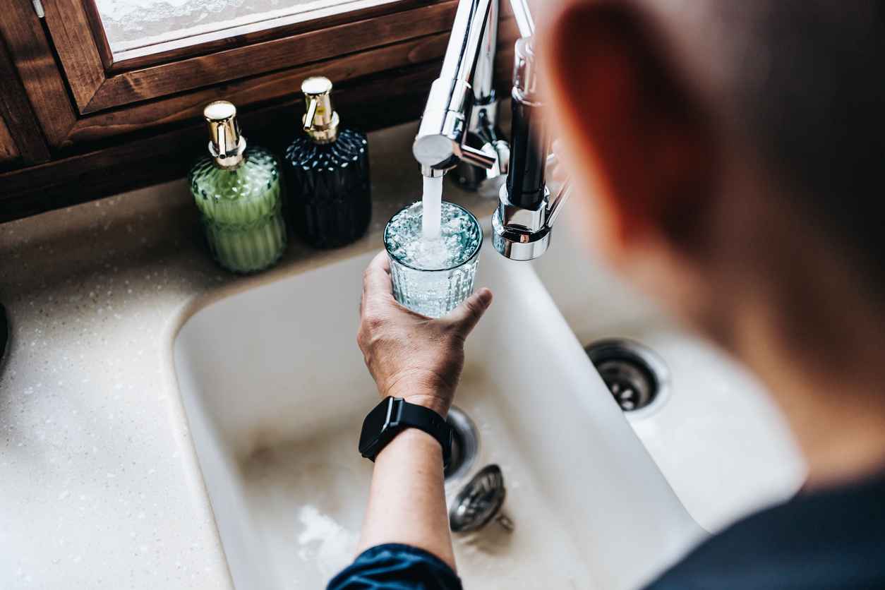 Over the shoulder view of a man filling a glass of filtered water right from the tap in the kitchen at home