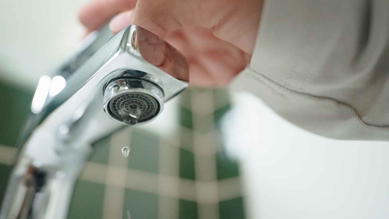 Close-up hand turning on or off faucet in bathroom.