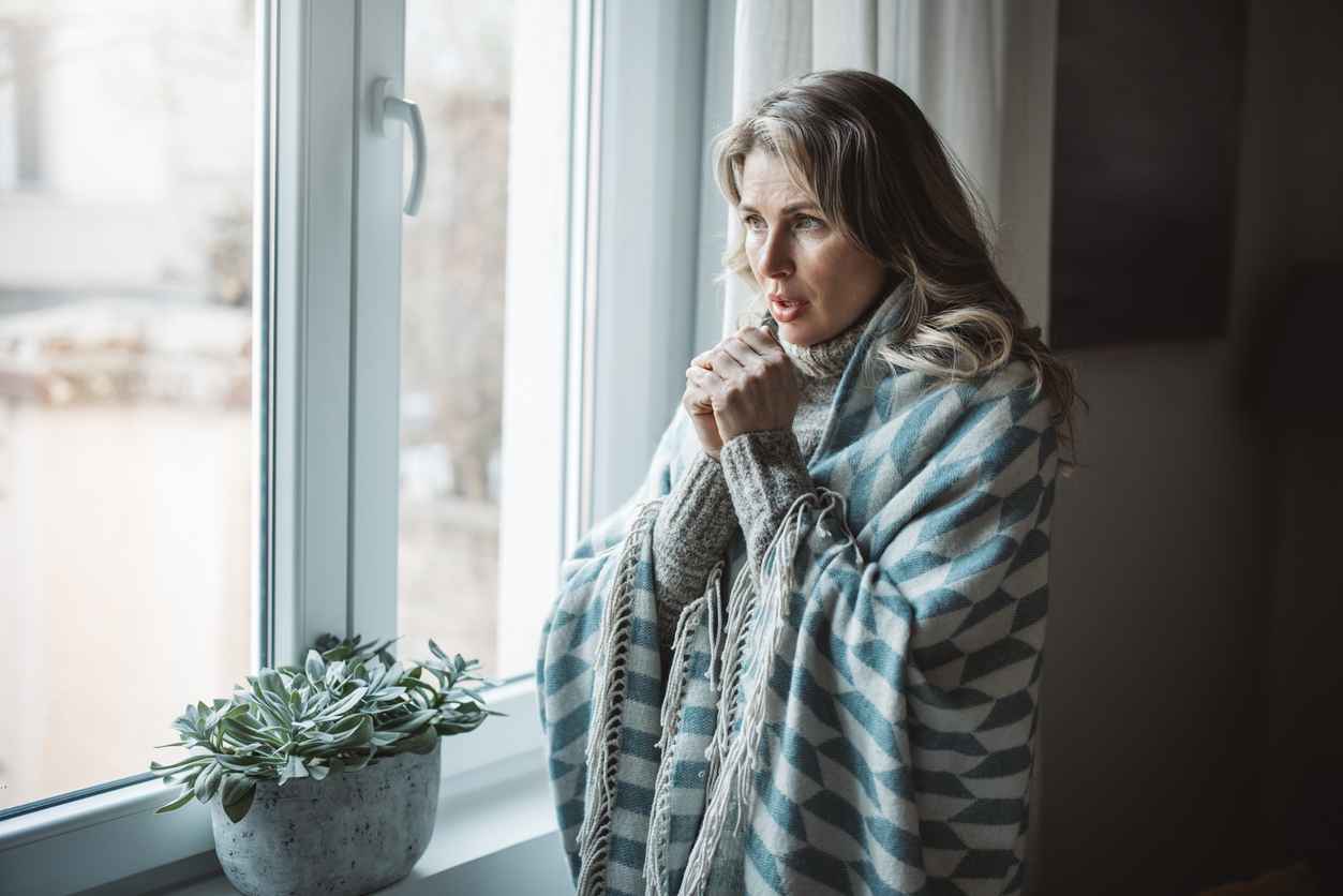 Woman standing in her home wrapped in a blanket due to a lack of heat in the room